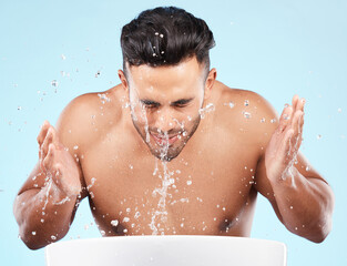 Face, water splash and skincare of man cleaning in studio isolated on a blue background. Hygiene,...