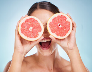 Face, beauty skincare and woman with grapefruit in studio isolated on a blue background. Organic cosmetics, healthy diet and happy female model holding fruit for vitamin c, facial care and wellness.
