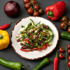 Salad of fresh vegetables, red beans and croutons on plate. Dark background is decorated with pepper, cherry tomatoes, onion, paprika. Vegetarian low calorie dish. Healthy diet. View from above.