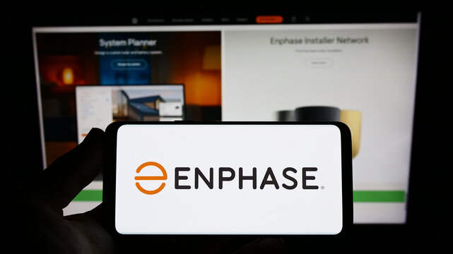 Stuttgart, Germany - 12-23-2022: Person holding smartphone with logo of US company company Enphase Energy Inc. on screen in front of website. Focus on phone display.