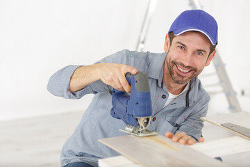 happy man with fret saw cutting wood plank at workshop