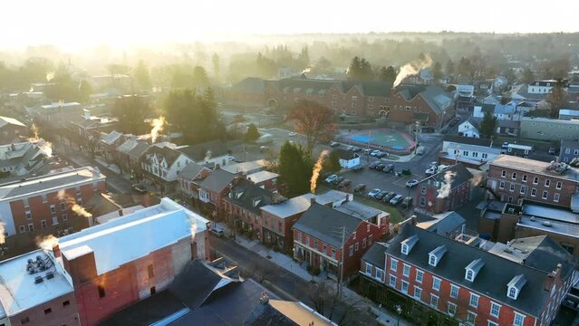 Small town USA in winter sunshine. Homes and school building with smoke from chimneys in cold season. Aerial view.