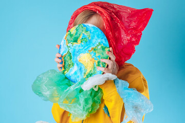 Creative concept plastic bag free. A child closing his face with a painting planet Earth on a blue background. Save nature. Save the ocean. Pollution and addiction to plastic.