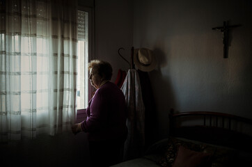 Portrait of old lady standing beside window in bedroom