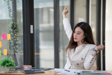 Young businesswoman stretching with hand raised while sitting on a chair in an office.