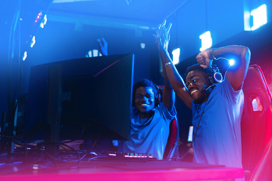 Professional african cyber gamer greeting and support team fists hands online game in neon blur background. Concept winners cybergame championship