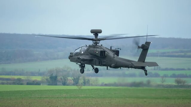British army Boeing Apache Attack helicopter gunship (AH-64E AH64E) hovers and rotates just above a grass meadow, Wiltshire UK