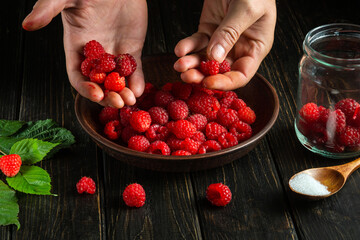 Chef sortings through fresh red raspberries in the kitchen to prepare a sweet soft drink. Cooking diet desserts cook's hands