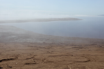 Atmospheric empty sea shore in early morning with fog above quiet water and sunlight on horizon with yellow sand beach and cape in haze. Zen and meditative landscape.