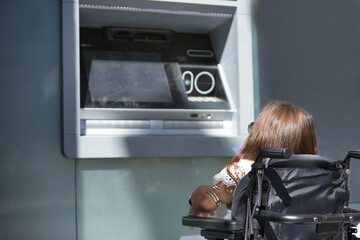 Disabled woman with reduced mobility and small stature in an electric wheelchair trying to withdraw...