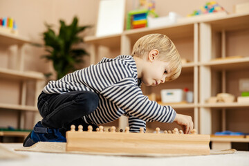 Modern development. A focused child is playing with wooden montessori toy and learning shapes.