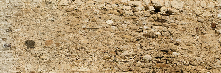 Ancient stone wall. Weathered rough masonry surface. The wall of the old castle. Wide panoramic texture for background and design.