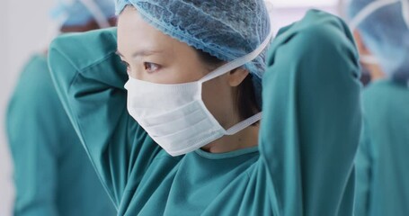 Video of asian female surgeon tying face mask in operating theatre, copy space - Powered by Adobe