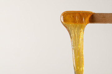 Liquid yellow sugar paste or wax for epilation on wooden stick or spatula closeup