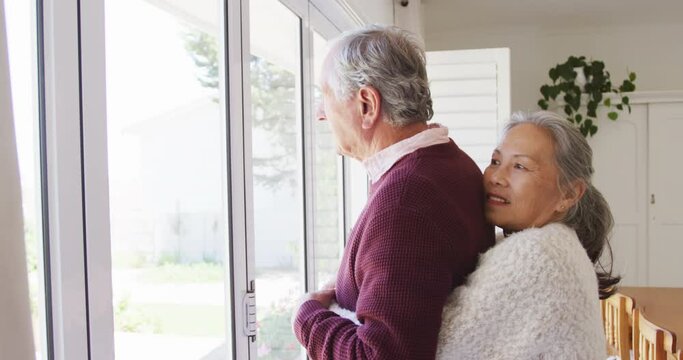 Happy diverse senior couple embracing and looking through window together