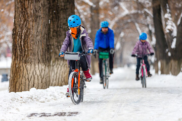 Father and children ride bicycles in winter. A man with his son and daughter ride bicycles along the bike path in the winter park