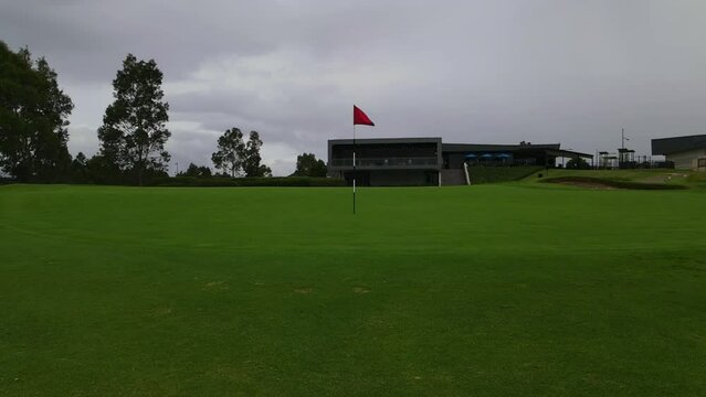 red golf pole flag on manicured green at golf course hole 18 by club house