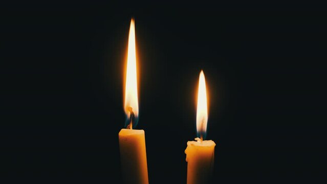 Two candles burn on a black background. A yellow flickering candles illuminates the darkness, close-up. Concept remembrance, religion, or celebration. The warm glow of flame sways. Isolated, Copyscape
