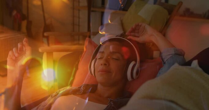 Animation of sunset landscape over biracial woman listening to music with headphones on