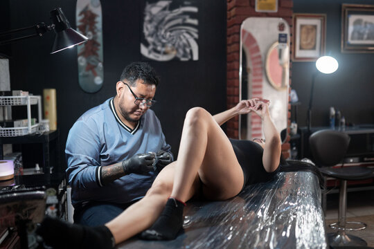 A tattoo artist is cleaning his machine while the woman client is texting with her phone
