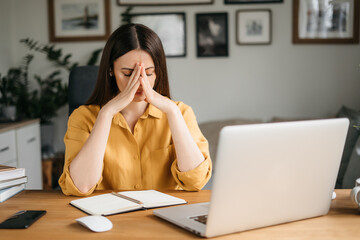 Female freelance with eyes closed is massaging head temples with suffering face expression. Tired...