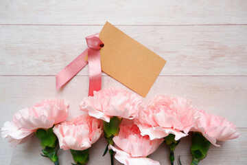 Beautiful pink carnation flowers decoration with blank message card on white wooden background. Pink Carnation floral background for Mother's day, women's day and wedding day design.