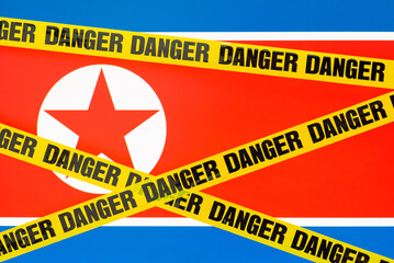 Flag of North Korea with danger tape on the foreground. Concept of dangerous travel to North Korea