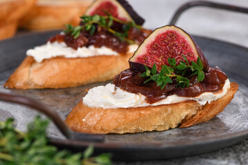  Canape or crostini with toasted baguette, cream cheese, onion jam, figs and fresh thyme on a tin tray. Ideal appetizer as an aperitif.