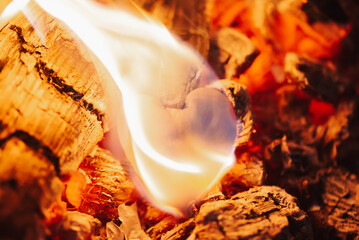 Hot coals and burning paper piece in the form of human heart, close up. Glowing and flaming coal, bright red fire and ash