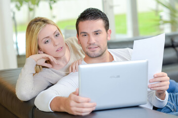 Couple looking at computer, holding sheet of paper