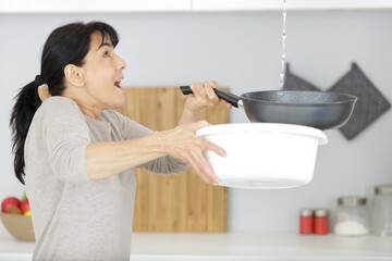 woman holding bucket while water droplets leak from ceiling