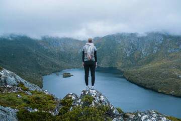 Woman stands on rock on top of mountain wearing a scarf looking over a lake and cloudy sky