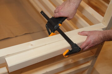 The carpenter fixes the wooden bars on furniture with a gun type clamp. Home carpentry