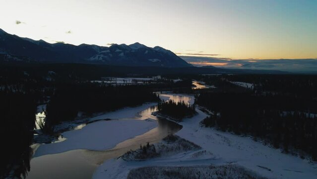 Aerial Approach Shot of Beautiful Winter Landscape During Golden Hour, Showing River with Reflection and Majestic Mountains in the Distance in British Columbia, Canada"