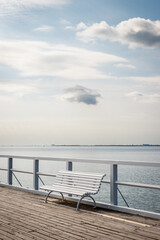 Empty white bench on pier at coastline Baltic sea. Tranquil scenery with clouds on sky