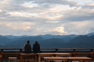 Two people looking at the mountain landscape view sitting with their backs to the camera
