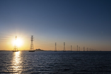 바다 위에 설치된 송전탑과 그 뒤로 떠오른 태양