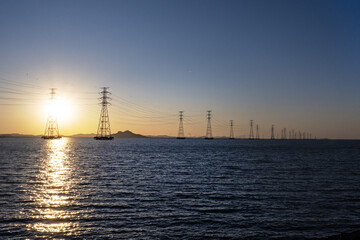 바다 위에 설치된 송전탑과 그 뒤에 떠있는 태양