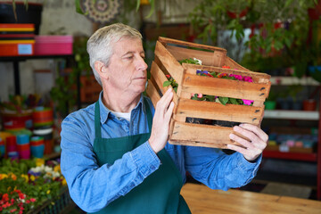 Gärtner trägt Kiste Pflanzen in der Gärtnerei für Lieferung - obrazy, fototapety, plakaty
