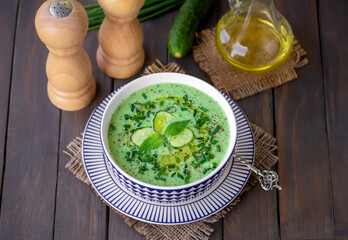 Cold Yogurt and Cucumber Soup topped with cucumber slice, olive oil and chopped scallion. Selective focus, horizontal, wooden table.