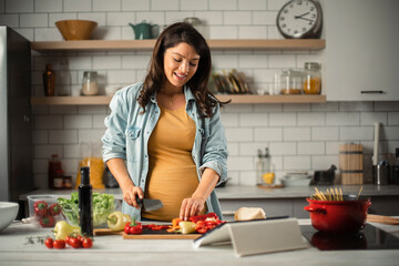 Beautiful pregnant woman preparing delicious food. Smiling woman preparing delicious food.