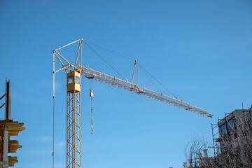 Tower crane between buildings in construction closeup on blue sky background