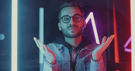 Portrait of young man vlogger speaking and pointing at camera recording video against neon light background. Vlogging and modern lifestyle concept.