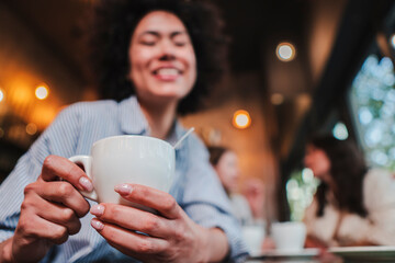 Close up portrait of one young happy woman holding an drinking a coffee cup in a restaurant. Isolated lady smiling with a latte mug on her hands. High quality photo