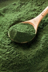 spirulina chlorella algae powder in a wooden spoon on green background.