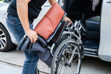 Obraz premium Asian woman folding and lift up wheelchair into her car. Accessibility concept.
