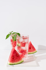 Dos vasos de zumo de sandía con trozos de sandia y hielo sobre fondo claro