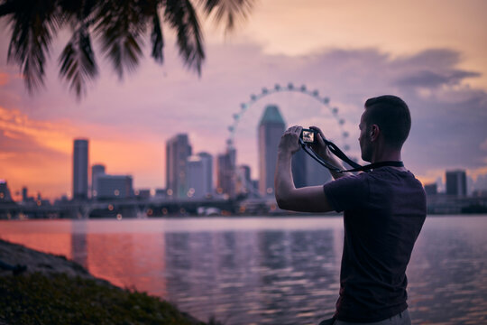 Man photographing Singapore urban skyline at beautiful sunset. Tourist with camera in modern city.