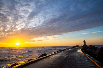 path to lighthouse on zuidpier IJmuiden at sunset with cloudy sky and sun above horizon