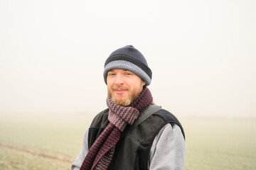 Fototapeta na wymiar portrait of a young man wearing a hat and scarf out walking in the countryside on a foggy winters morning